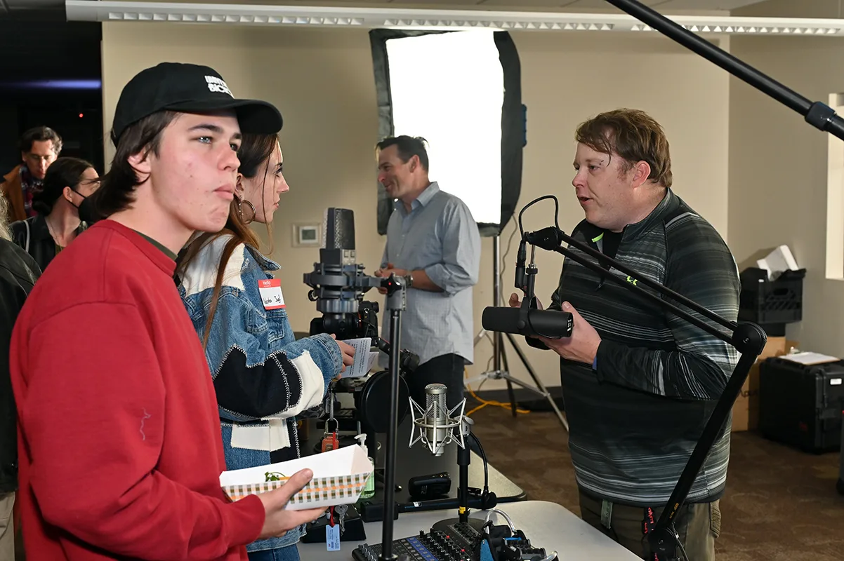 Attendees trying out cameras and a boom-mounted microphone at a gear demo, with a softbox light behind them, at the Boulder County Film Commission fall event