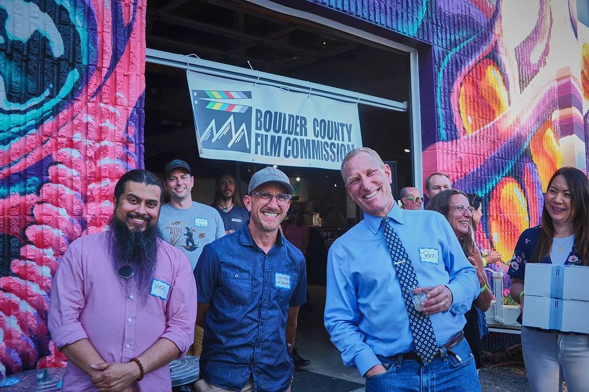 Smiling attendees in front of the Boulder County Film Commission banner and a colorful mural at the launch event