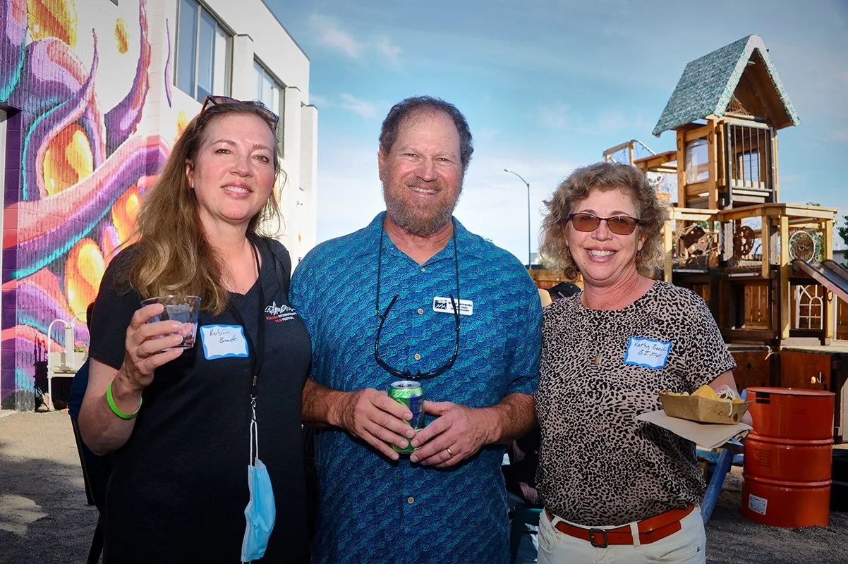 Three smiling attendees with name tags at the Boulder County Film Commission launch event, with a wooden playground structure behind them