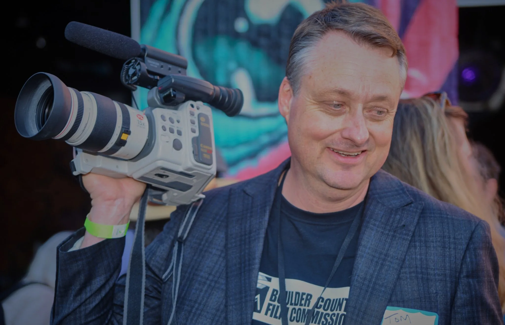 Man in a Boulder County Film Commission T-shirt holding a vintage camcorder at the launch event