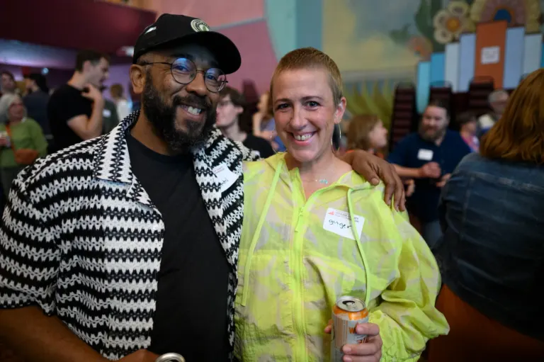 Two smiling attendees with their arms around each other at a crowded Boulder County Film Commission Schmoozer