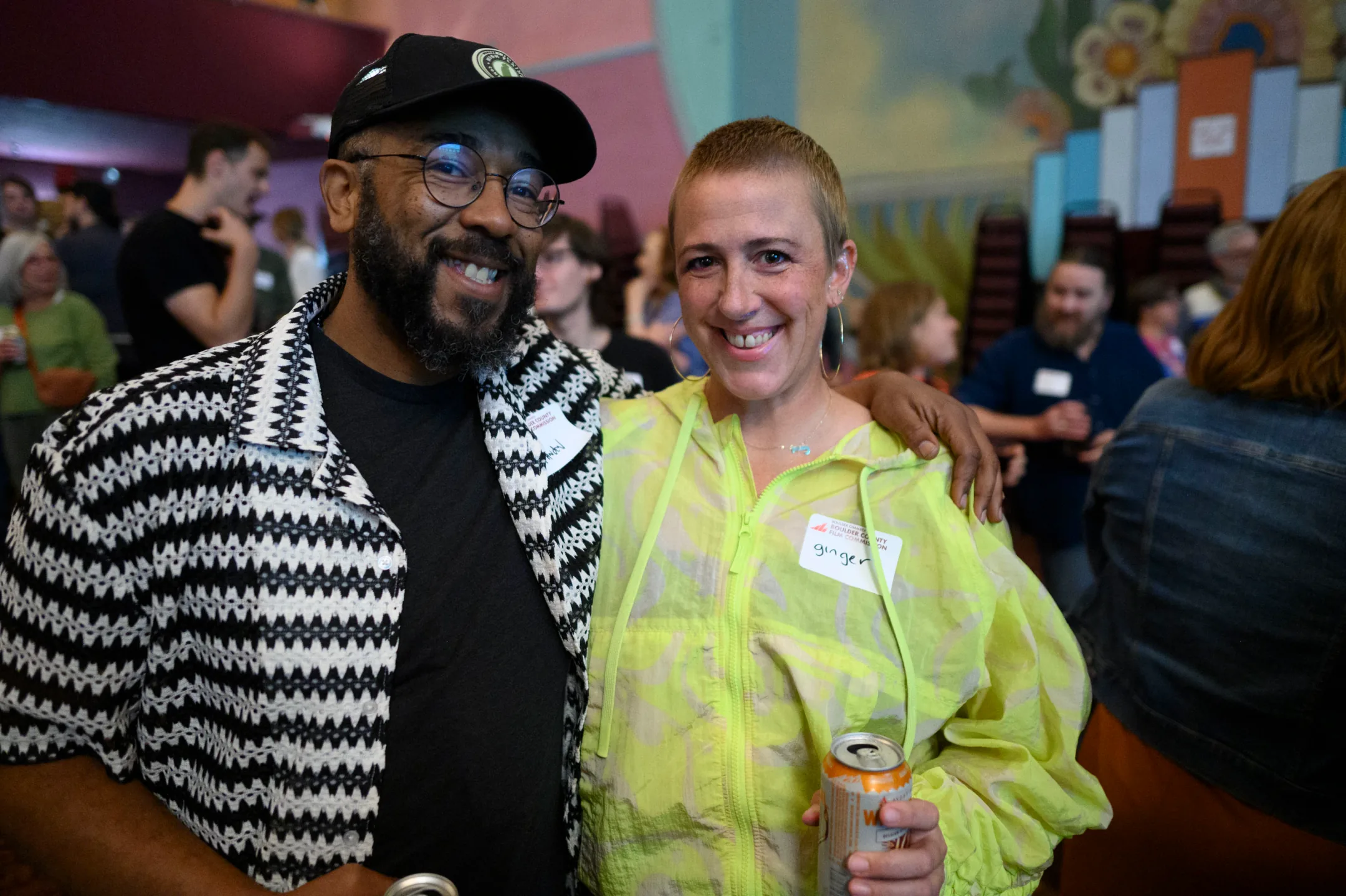 Two smiling attendees with their arms around each other at a crowded Boulder County Film Commission Schmoozer