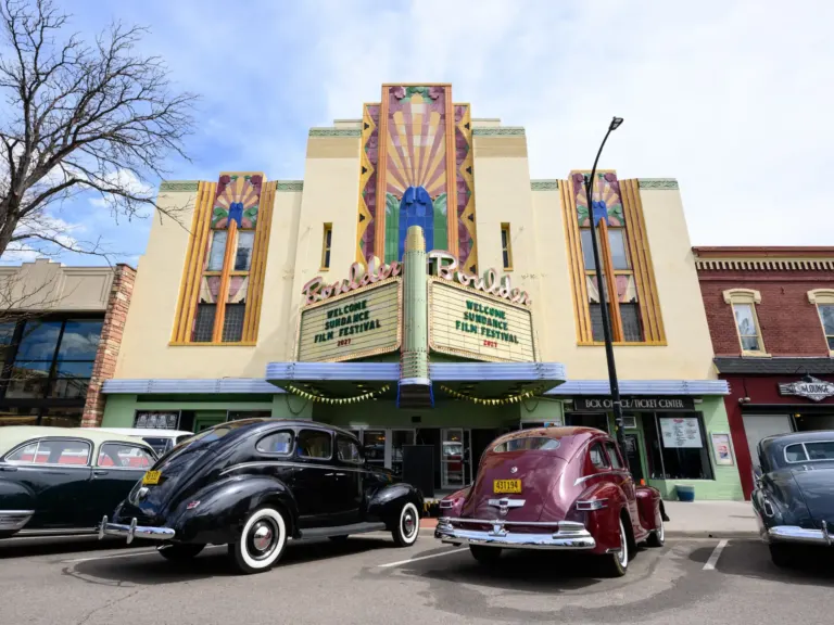 The art deco Boulder Theater, its marquee welcoming the Sundance Film Festival 2027, with vintage cars parked out front