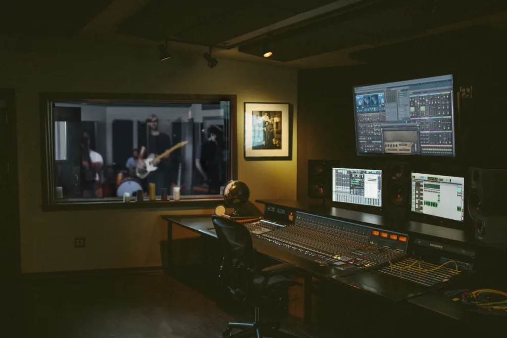Coupe Studios control room with a mixing console and monitors, looking through the window into a live room where a band is recording