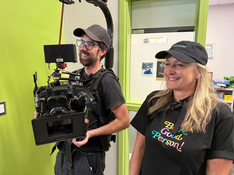 Camera operator wearing a cinema camera rig beside a smiling director in a cap