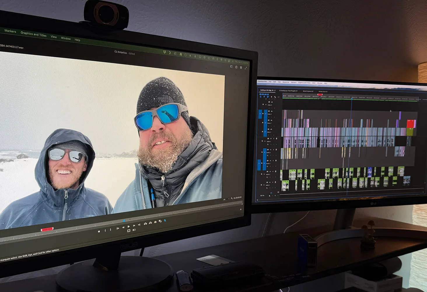 Editing workstation with one monitor showing two men in winter gear on a snowy shore and another showing an editing timeline