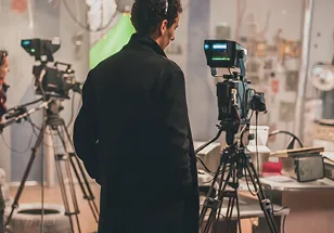A camera operator working behind a professional video camera on a tripod at an indoor production set