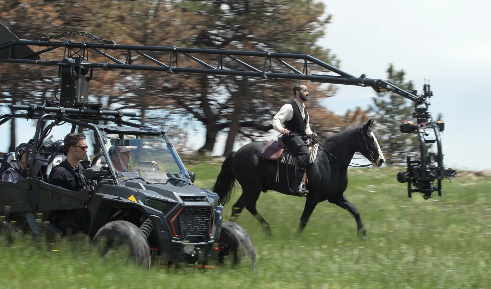 Rider on a black horse being filmed by a camera crane mounted on an off-road vehicle in a meadow