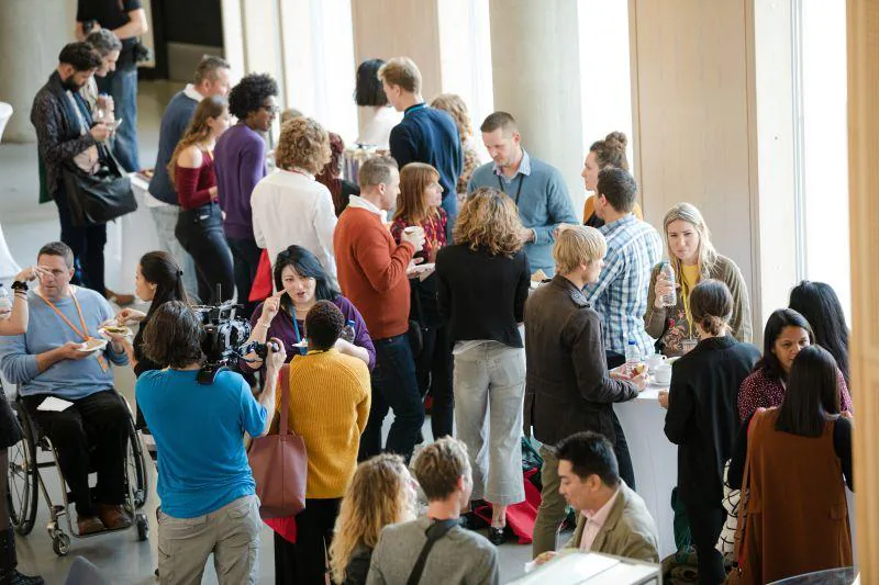 Attendees mingling at a networking reception in a bright atrium while a camera operator films