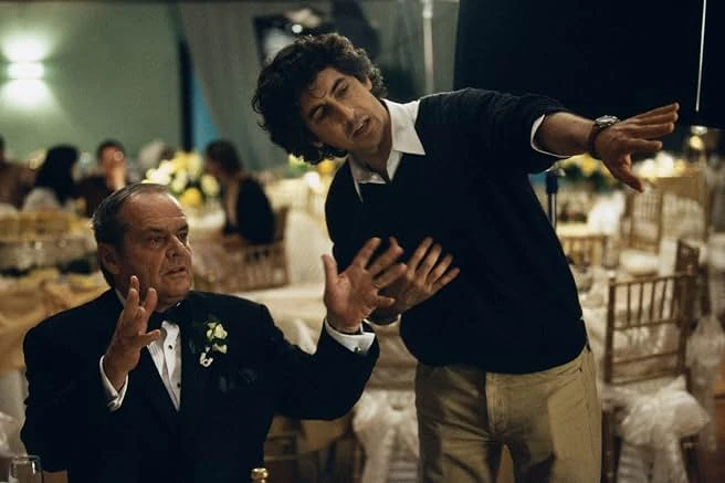 On a wedding reception set, an actor in a tuxedo gestures as a man in a dark sweater points off camera.