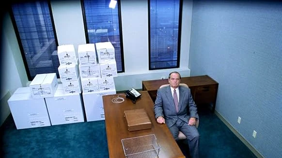 Warren Schmidt sits alone at a bare desk in an emptied office, with packed file boxes stacked by the windows.