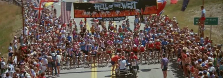 Cyclists pack the start line under a Hell of the West banner on a road lined with spectators and flags