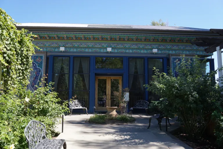 Blue-framed teahouse front with a painted cornice and wooden doors, seen along a garden walk with iron benches.