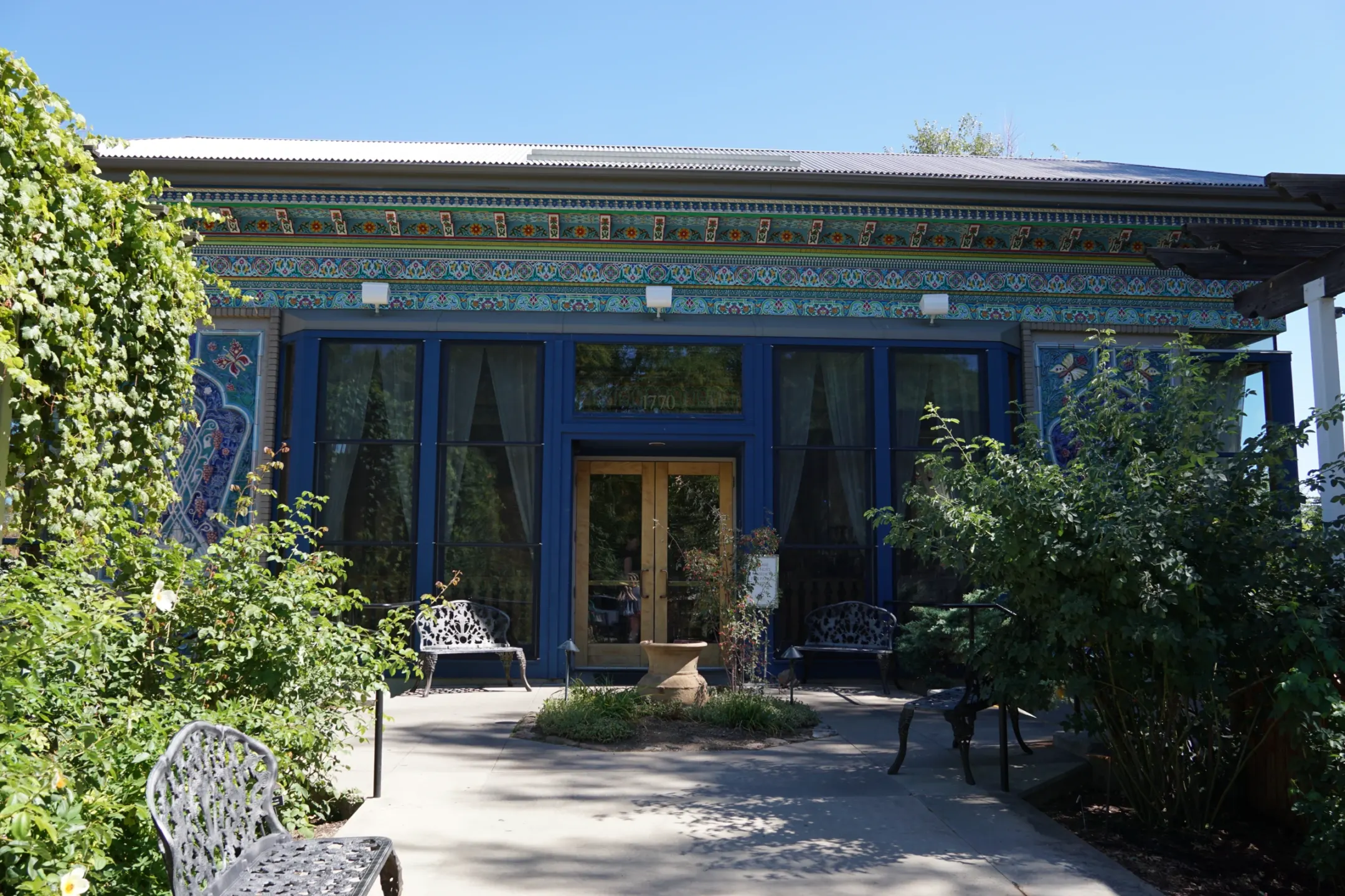 Blue-framed teahouse front with a painted cornice and wooden doors, seen along a garden walk with iron benches.