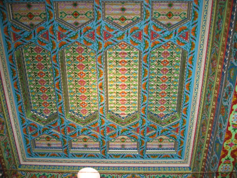 Painted wooden ceiling with four long recessed panels of pink and orange flowers, framed by sky-blue beams with orange blossoms.
