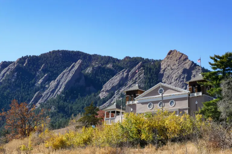 Chautauqua Auditorium's gabled front and shingled towers above yellow fall brush, with the Flatirons behind under a blue sky