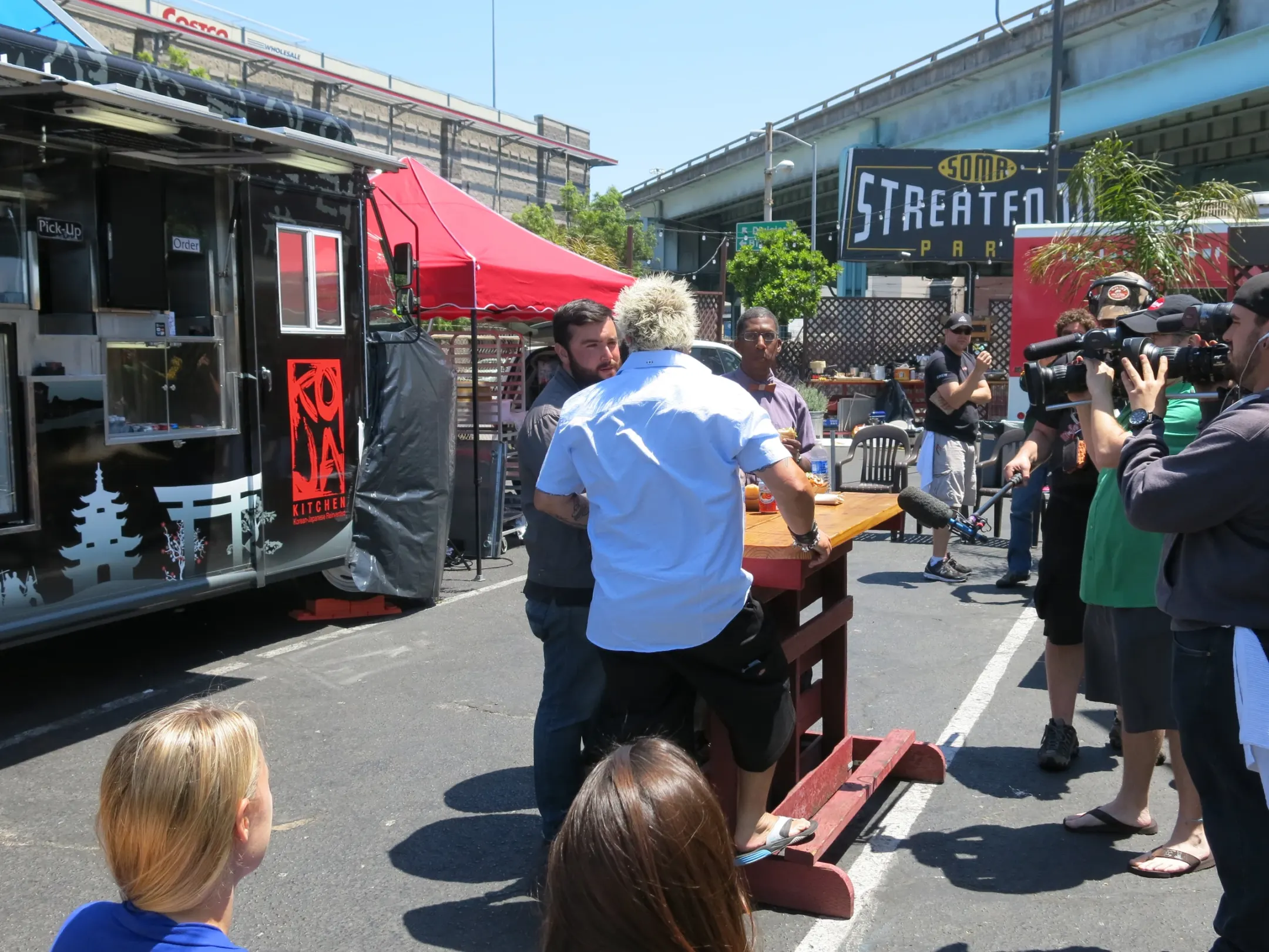 Guy Fieri at a food truck table as a camera operator and boom mic film him under the SoMa StrEat Food Park sign