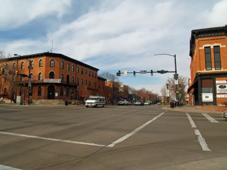 Wide intersection with a three-story red brick hotel on the left corner, traffic signals overhead and storefronts receding behind bare trees.