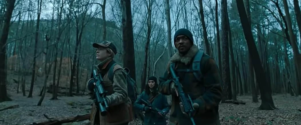 Three people with rifles stand watch in a forest of bare gray trees, a man in a knit cap and fur collar at right