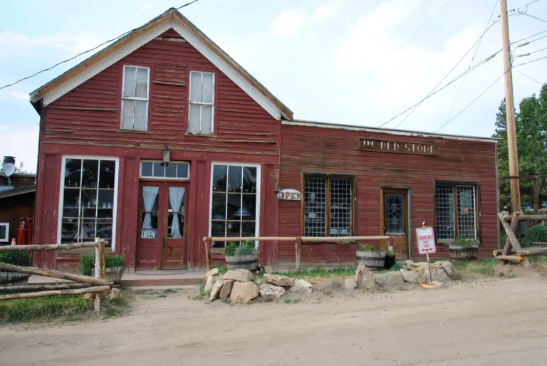 Weathered red clapboard storefront signed The Red Store beside a gravel street, with log rail fences and a utility pole