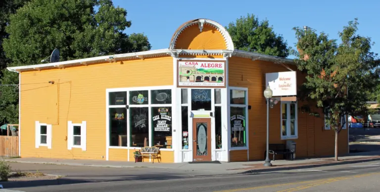 Orange wood-frame corner building with white trim and a sunburst arch above its angled entrance, beside an empty street in morning sun.