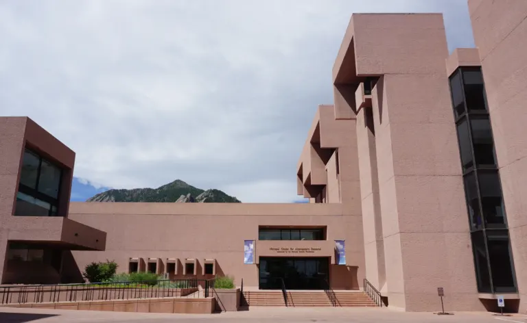 Paved court, steps and ramp leading to the main entrance of the NCAR Mesa Laboratory, with a concrete tower at right and a peak beyond