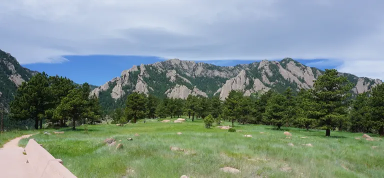 Green meadow with boulders and ponderosa pines below the Flatirons, seen from beside a pink concrete wall at the NCAR Mesa Laboratory
