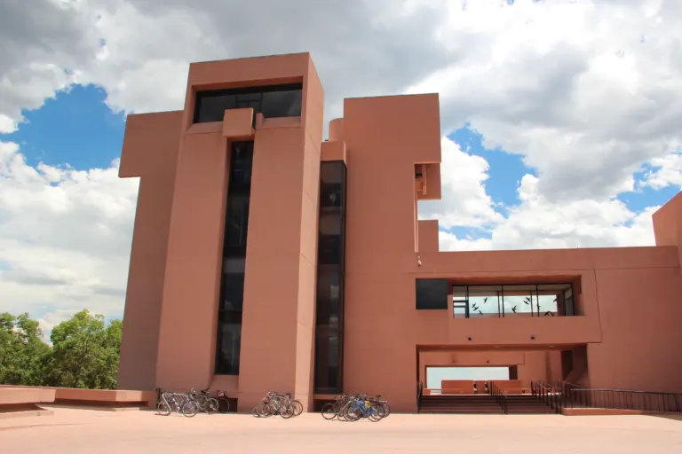 Pink concrete tower of the NCAR Mesa Laboratory above a paved plaza, with bicycles parked at its base under a cloudy sky