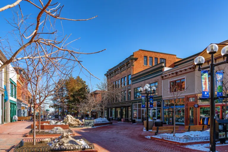 Ornate three-story brick storefronts beside a brick pedestrian mall with bare trees, globe street lamps and melting snow under a blue sky.