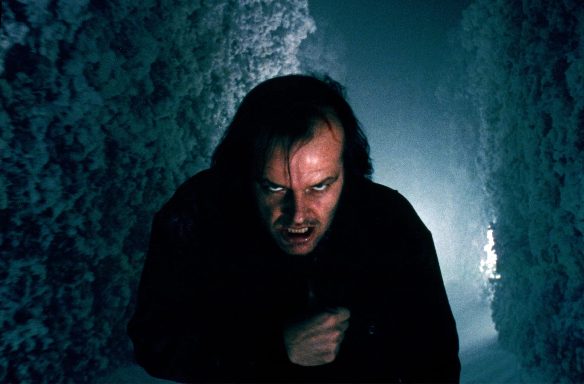 Jack Torrance, hair wild and teeth bared, staggers toward the camera through the snow-covered hedge maze at night