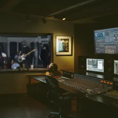 Coupe Studios control room with a mixing console and monitors, looking through the window into a live room where a band is recording
